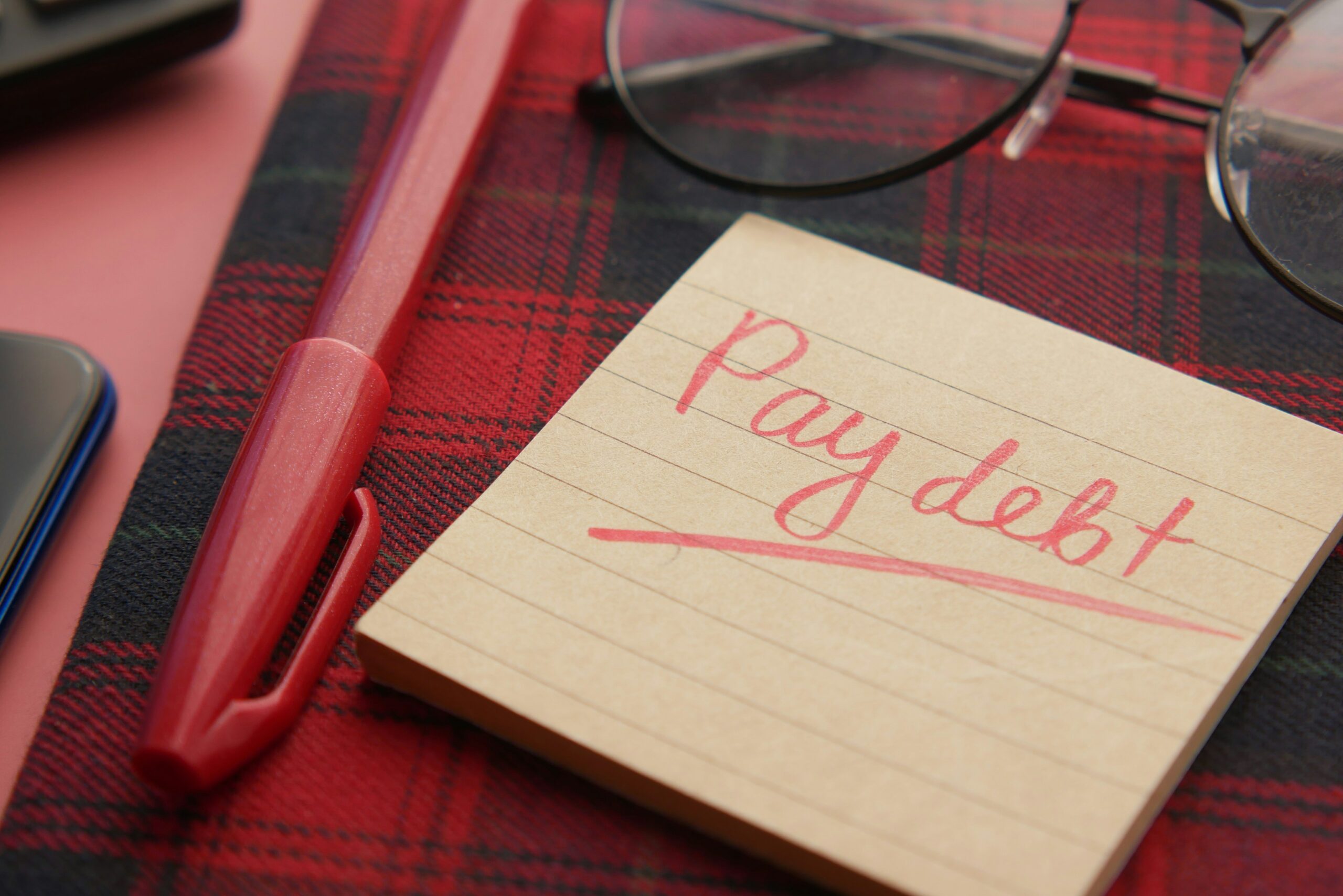 Notepad with "Pay debt" written in red pen representing debt consolidation credit management goals